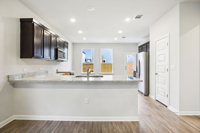 kitchen with light stone countertops, appliances with stainless steel finishes, sink, and light hardwood / wood-style floors