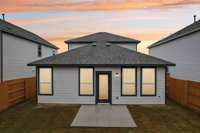 back house at dusk featuring a patio and a yard