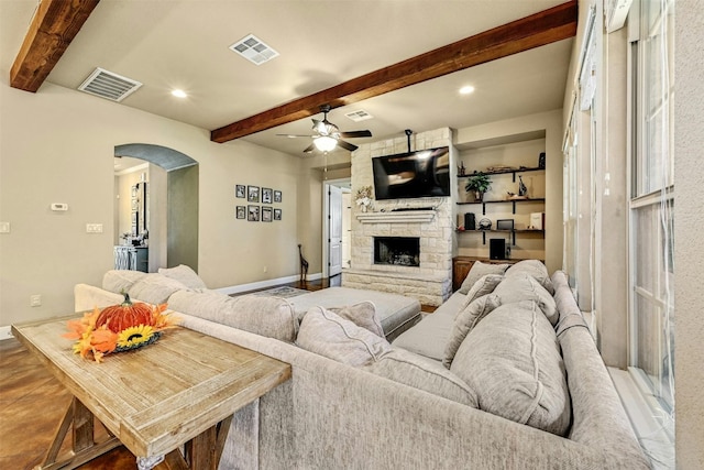 living room with beamed ceiling, ceiling fan, and a stone fireplace