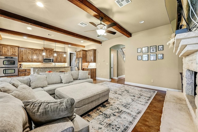 living room with ceiling fan, a fireplace, beamed ceiling, and dark tile patterned flooring