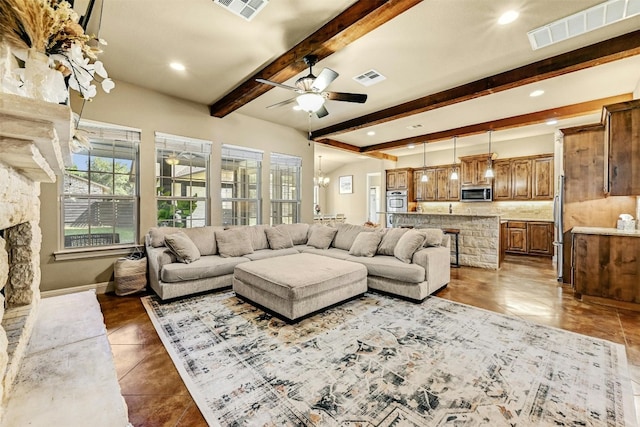 living room with beamed ceiling, ceiling fan, a stone fireplace, and dark tile patterned floors