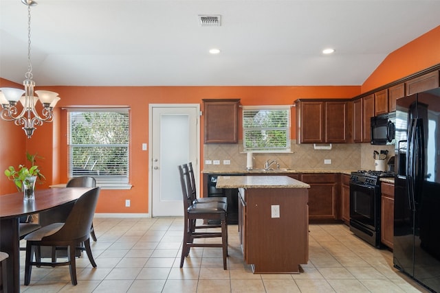 kitchen with lofted ceiling, hanging light fixtures, a kitchen island, black appliances, and light stone counters