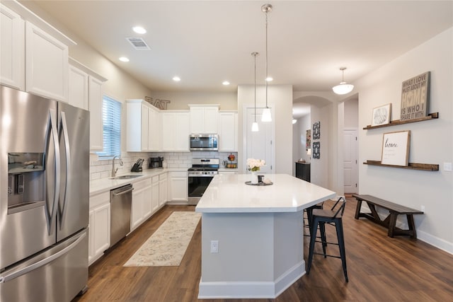 kitchen with a kitchen island, dark wood-type flooring, pendant lighting, white cabinetry, and appliances with stainless steel finishes