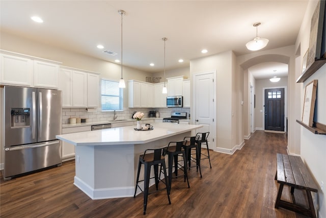 kitchen with white cabinets, hanging light fixtures, a kitchen island, appliances with stainless steel finishes, and dark wood-type flooring