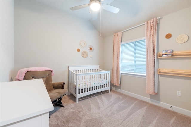 bedroom featuring light carpet, a nursery area, and ceiling fan