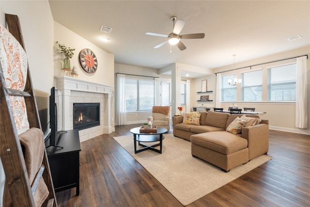 living room with dark wood-type flooring, a tiled fireplace, and ceiling fan with notable chandelier