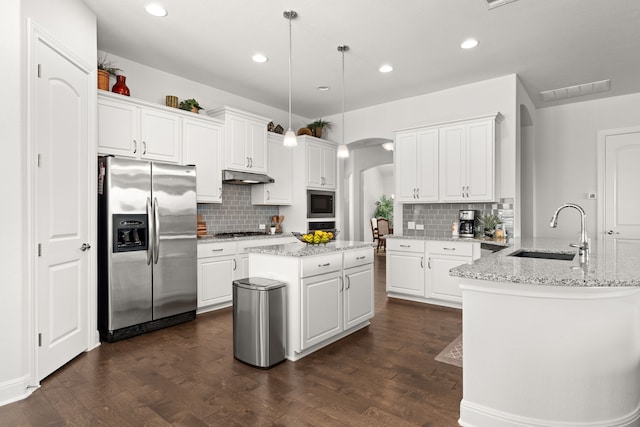 kitchen featuring stainless steel appliances, pendant lighting, light stone counters, a kitchen island, and sink