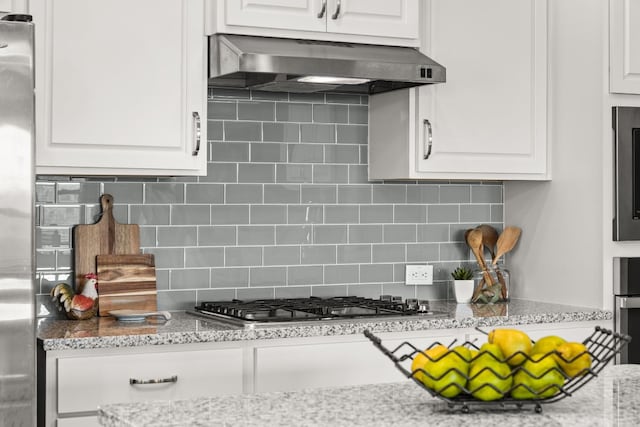 kitchen with exhaust hood, stainless steel gas cooktop, light stone counters, white cabinets, and backsplash