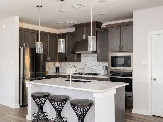 kitchen featuring a breakfast bar area, backsplash, stainless steel appliances, an island with sink, and decorative light fixtures