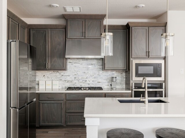 kitchen featuring sink, a breakfast bar area, decorative light fixtures, stainless steel appliances, and range hood