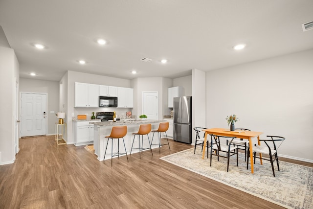 kitchen with a center island with sink, black appliances, a breakfast bar, white cabinets, and light hardwood / wood-style floors