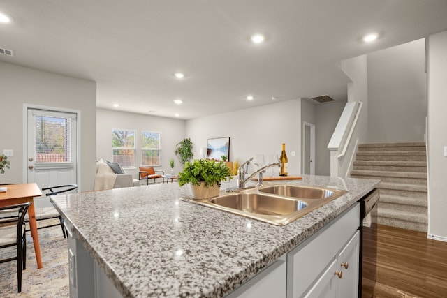 kitchen featuring a kitchen island with sink, wood-type flooring, sink, white cabinets, and light stone counters