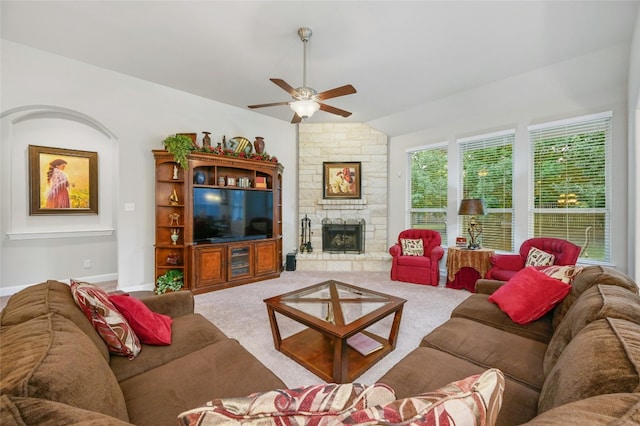 living room featuring carpet flooring, ceiling fan, a stone fireplace, and vaulted ceiling