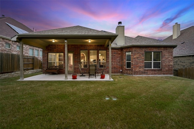 back house at dusk featuring a patio and a lawn