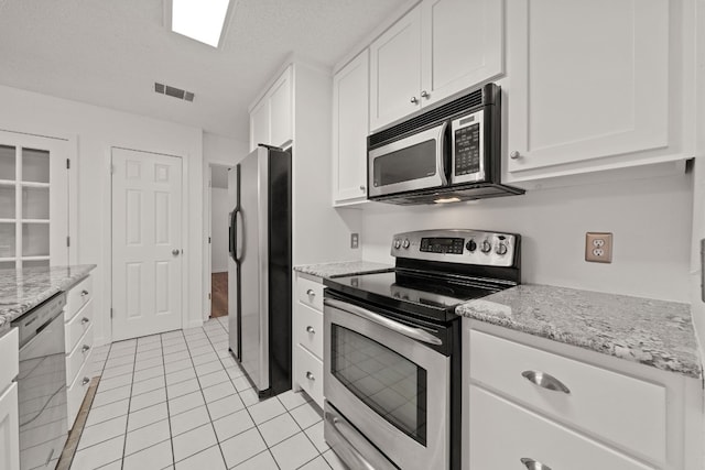 kitchen featuring appliances with stainless steel finishes, white cabinetry, light stone countertops, and light tile patterned flooring