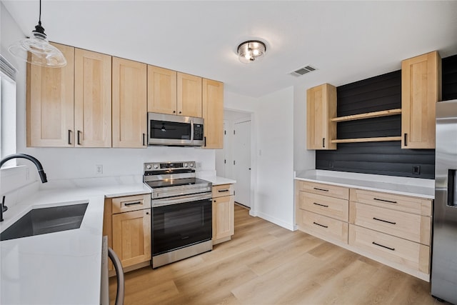 kitchen with light brown cabinetry, appliances with stainless steel finishes, decorative light fixtures, and light hardwood / wood-style floors