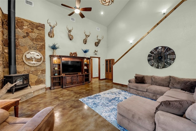 living room with ceiling fan, high vaulted ceiling, a wood stove, and concrete flooring