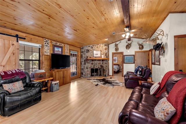 living room with vaulted ceiling with beams, a stone fireplace, ceiling fan, wooden ceiling, and light hardwood / wood-style flooring