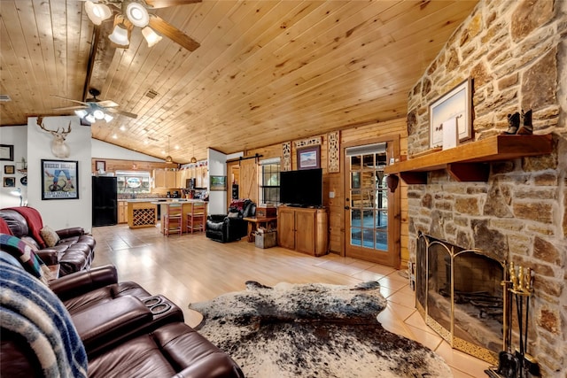 tiled living room with ceiling fan, a stone fireplace, vaulted ceiling, and plenty of natural light