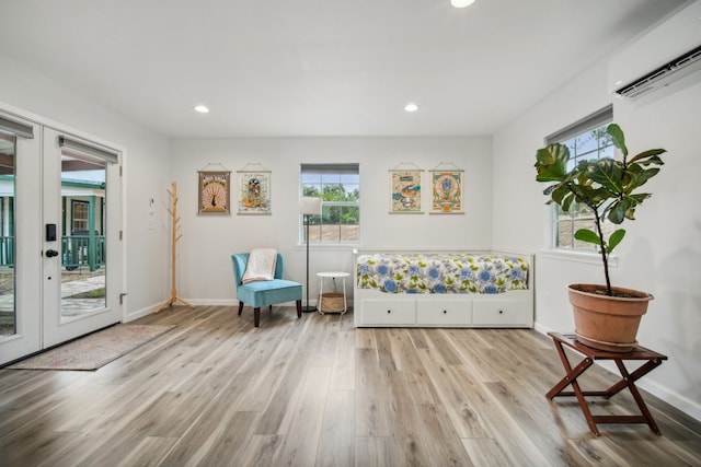 sitting room with french doors, a wall mounted AC, and light wood-type flooring