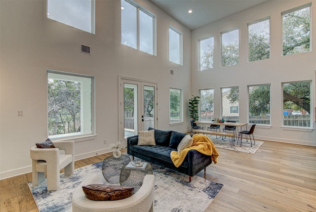 living room featuring french doors, a towering ceiling, plenty of natural light, and light hardwood / wood-style flooring