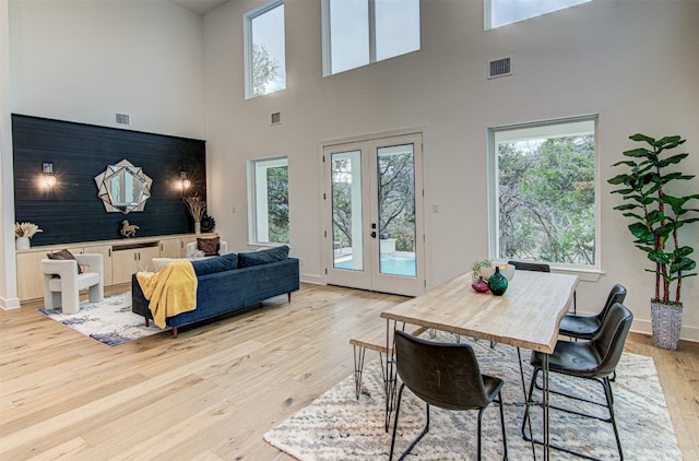 dining space with a towering ceiling, french doors, and light hardwood / wood-style flooring