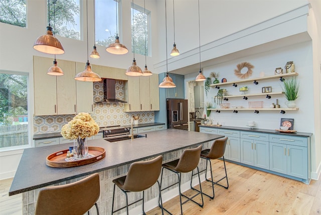 kitchen with a towering ceiling, backsplash, high end fridge, wall chimney exhaust hood, and sink