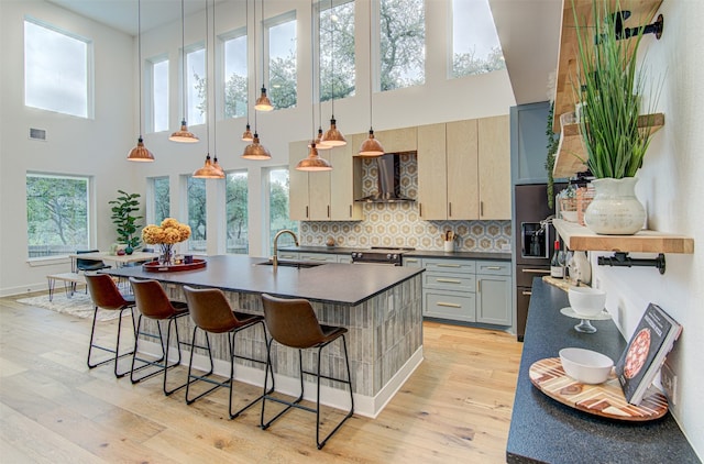 kitchen featuring a towering ceiling, tasteful backsplash, wall chimney exhaust hood, sink, and hanging light fixtures