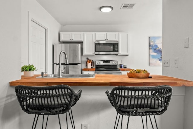 5616 Emerald Forest Dr Unit 101, Austin, TX 78745 - kitchen featuring appliances with stainless steel finishes, butcher block counters, white cabinets, a breakfast bar area, and a peninsula