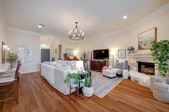 living room with wood-type flooring, ornamental molding, a chandelier, and a fireplace