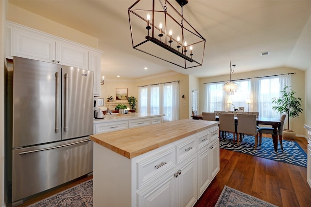 kitchen featuring high end fridge, butcher block countertops, a center island, pendant lighting, and white cabinets