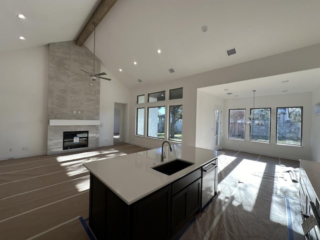 kitchen with dishwasher, a center island with sink, sink, hanging light fixtures, and a large fireplace