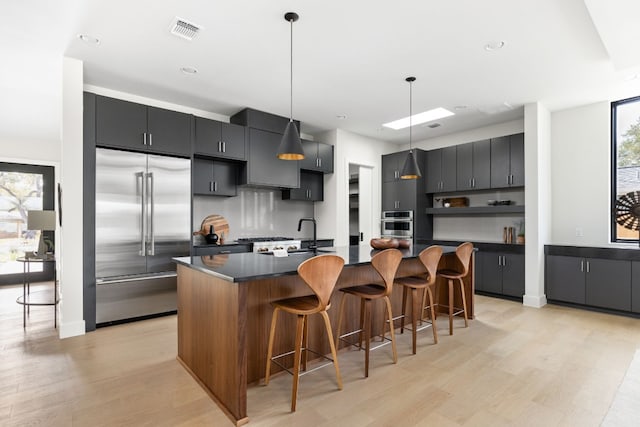 kitchen featuring hanging light fixtures, stainless steel appliances, a wealth of natural light, and an island with sink