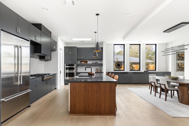 kitchen featuring sink, hanging light fixtures, appliances with stainless steel finishes, a kitchen island, and light wood-type flooring