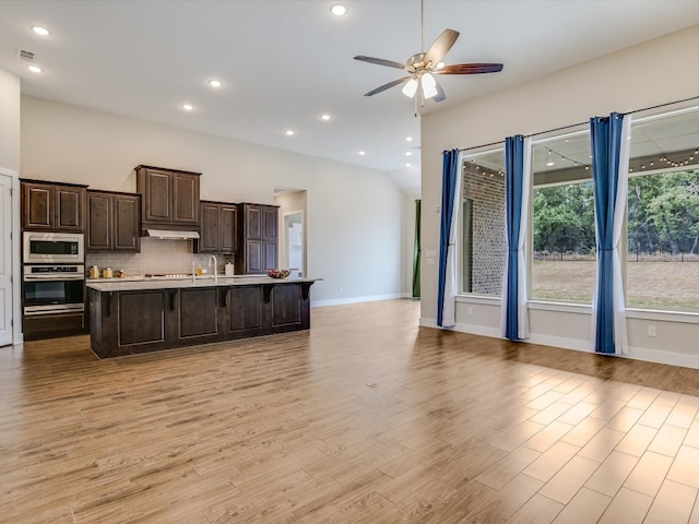 kitchen featuring stainless steel appliances, light wood-type flooring, an island with sink, a breakfast bar, and ceiling fan