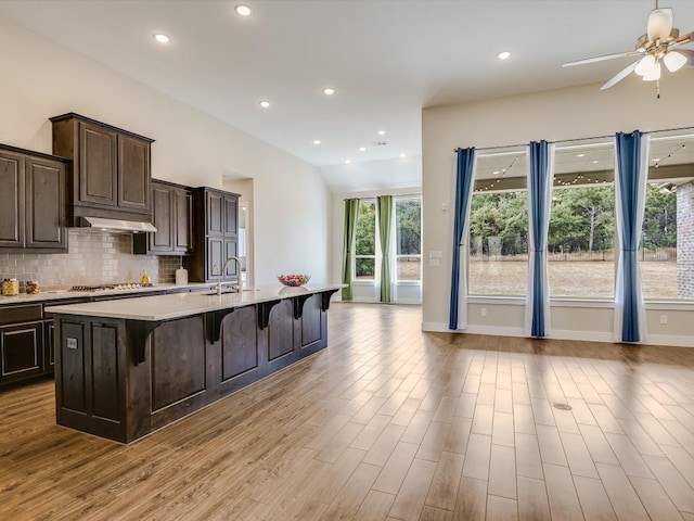 kitchen featuring a center island with sink, sink, decorative backsplash, a breakfast bar area, and light hardwood / wood-style flooring