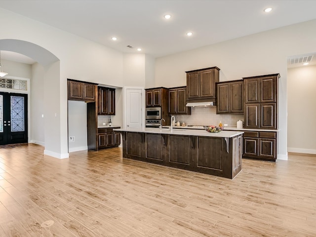 kitchen featuring dark brown cabinetry, a kitchen island with sink, a breakfast bar area, and light wood-type flooring