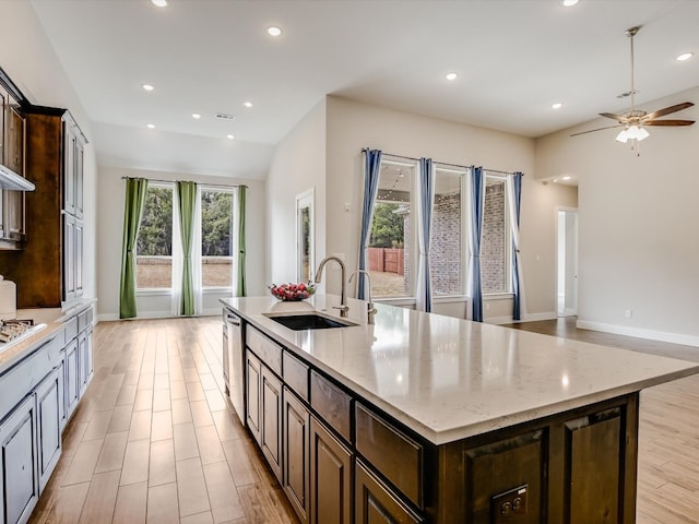 kitchen featuring light hardwood / wood-style floors, a center island with sink, sink, stainless steel dishwasher, and light stone countertops