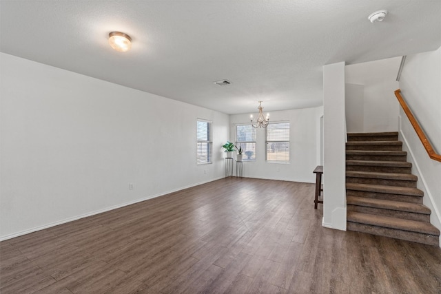 unfurnished living room with dark wood-type flooring, a textured ceiling, and an inviting chandelier