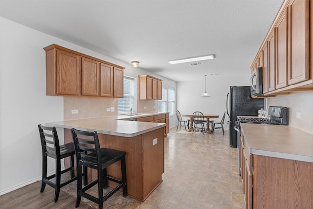 kitchen with sink, black stove, kitchen peninsula, pendant lighting, and a breakfast bar