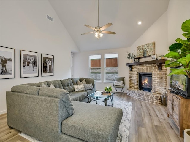 living room featuring a fireplace, light hardwood / wood-style floors, high vaulted ceiling, and ceiling fan