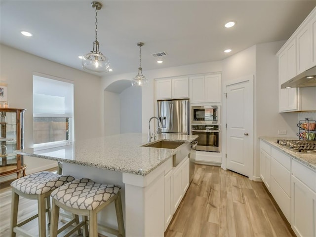 kitchen featuring light hardwood / wood-style flooring, decorative light fixtures, a kitchen island with sink, white cabinets, and appliances with stainless steel finishes