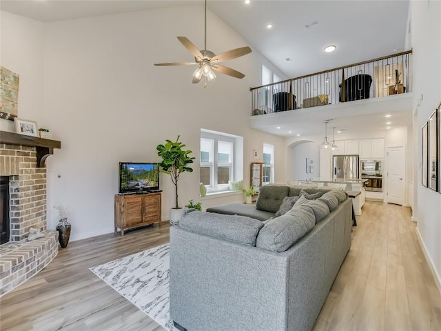 living room featuring ceiling fan, a fireplace, high vaulted ceiling, and light wood-type flooring