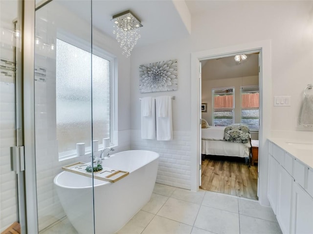 bathroom featuring an inviting chandelier, tile patterned floors, a bathtub, vanity, and tile walls