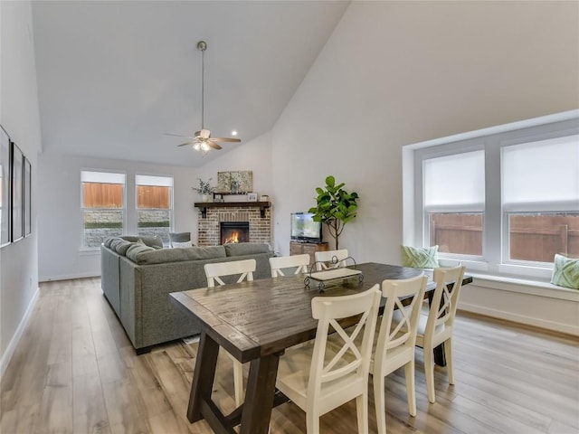 dining area featuring ceiling fan, high vaulted ceiling, light hardwood / wood-style floors, and a brick fireplace