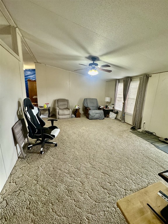 sitting room with a textured ceiling, vaulted ceiling, carpet flooring, and ceiling fan