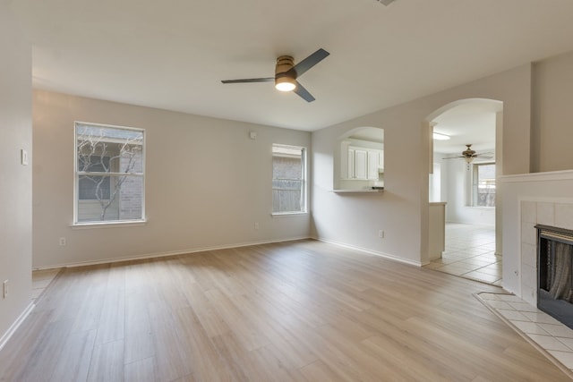 unfurnished living room featuring a tiled fireplace, ceiling fan, and light wood-type flooring