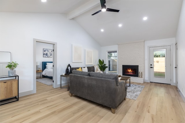 living room featuring high vaulted ceiling, ceiling fan, light wood-type flooring, a fireplace, and beamed ceiling