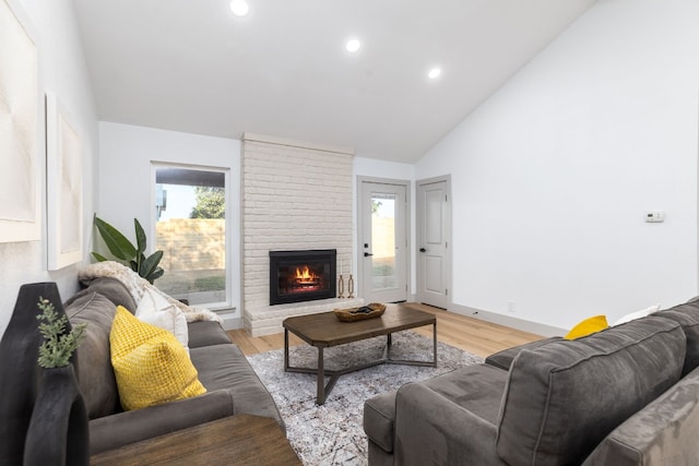 living room featuring a brick fireplace, high vaulted ceiling, a healthy amount of sunlight, and light hardwood / wood-style floors