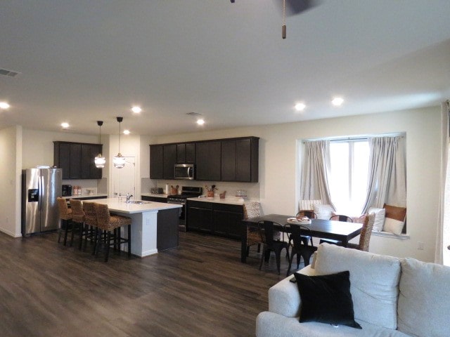 kitchen with dark wood-type flooring, a center island with sink, sink, hanging light fixtures, and stainless steel appliances